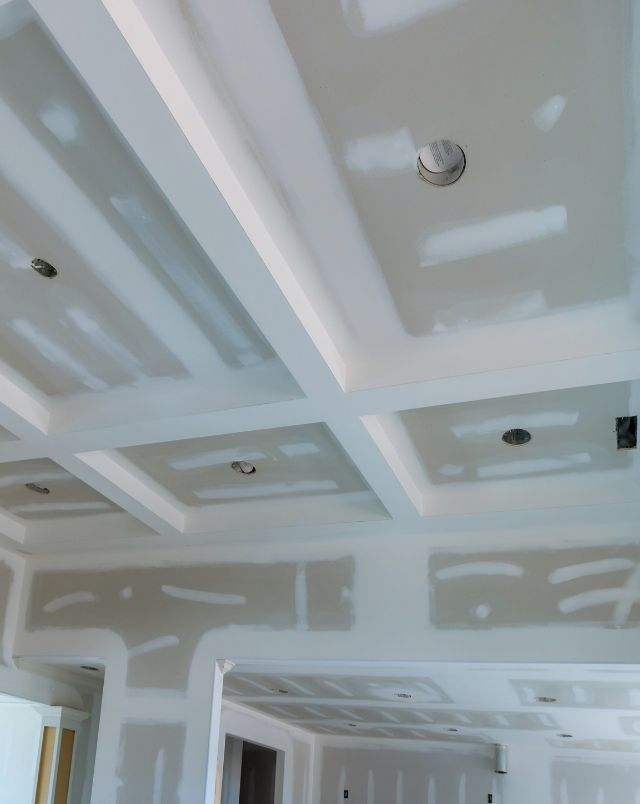 New construction interior showing drywall installation coffered ceiling spacious living area