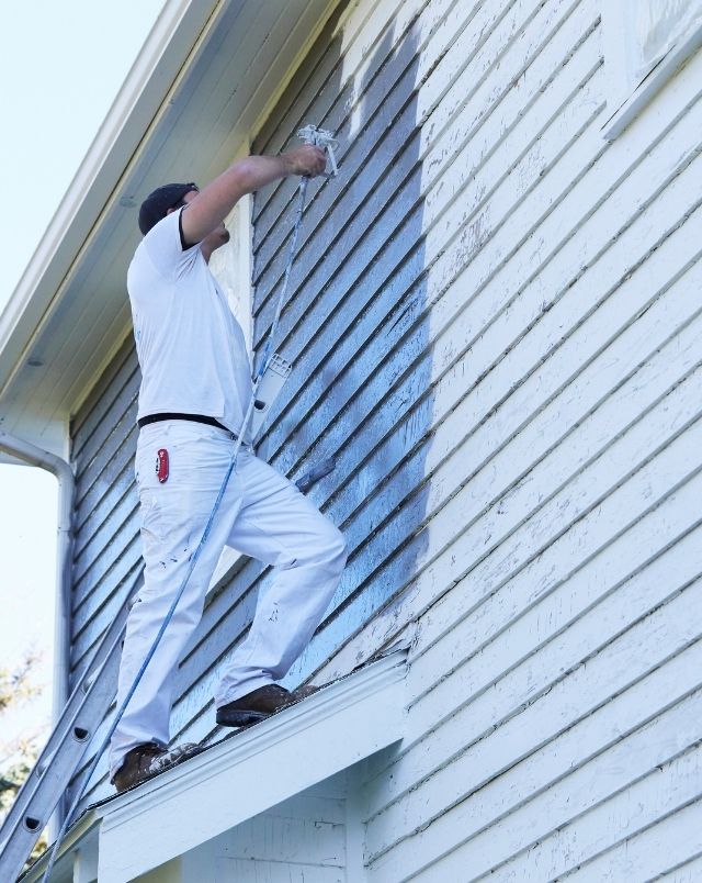 Painter Spraying Paint On Exterior of Old Home